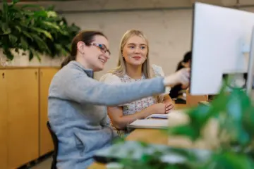 Two female employees in Codema look at a computer screen while one points something out. There are plants in the background.