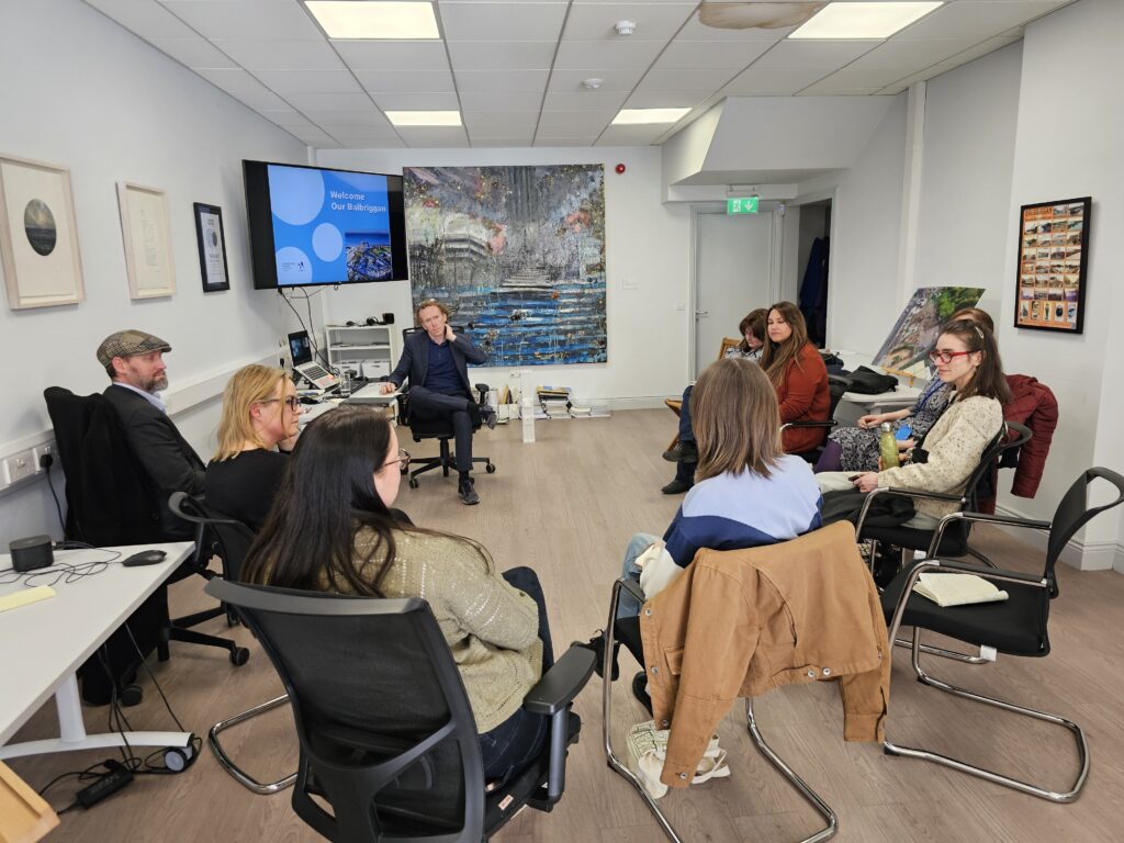 Members of Codema, Fingal County Council and Balbriggan SEC attending a meeting at the Our Balbriggan Hub, sitting in a circle, a TV screen reads 'Welcome to Our Balbriggan'