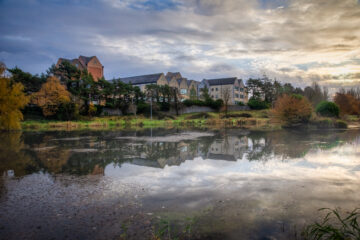 Picture of a river with buildings and trees in the background reflected in the water
