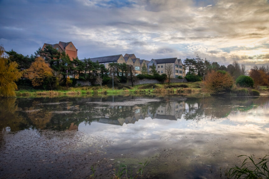 Picture of a river with buildings and trees in the background reflected in the water