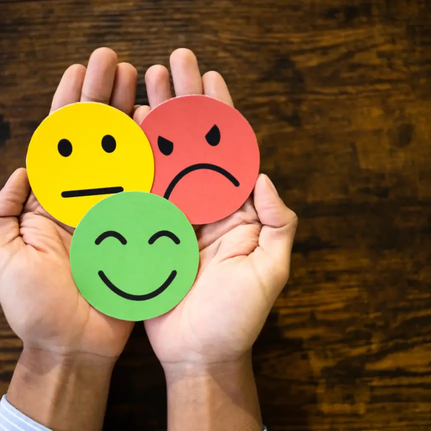 Image of hands holding emojis of happy, sad and inbetween expressions.