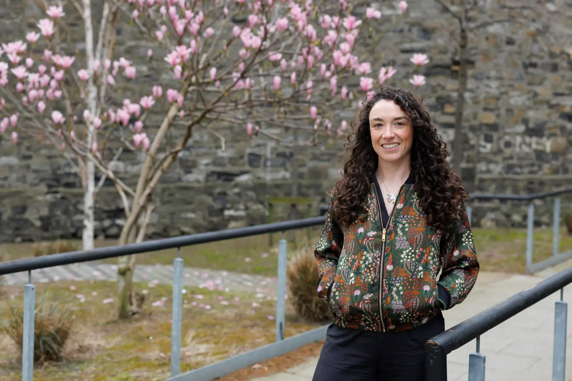 Pictured is Donna Gartland, CEO of Codema. She is outside The Grainstore building at The Digital Hub, there is an accessible ramp and a tree with pink magnolia leaves in the background.