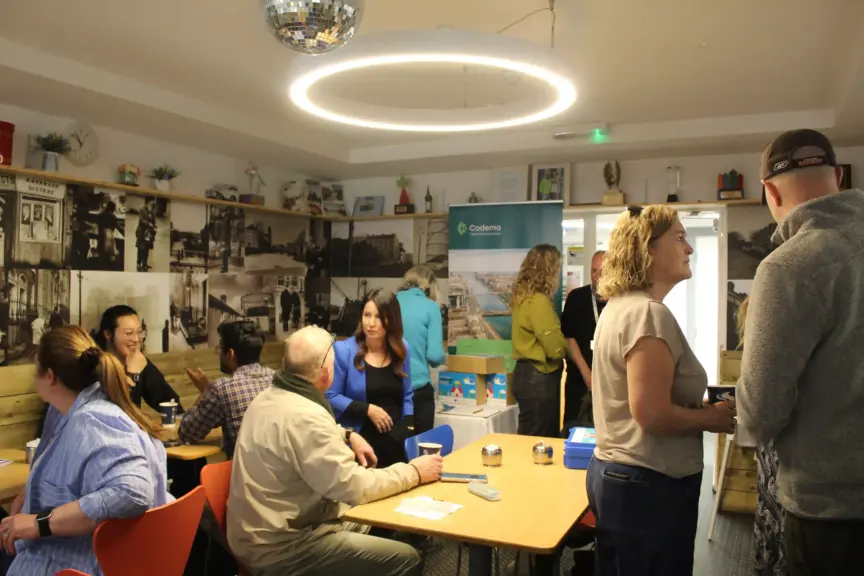 There are many people pictured at the launch of the Raytown Energy Dock in the cafe of the Ringsend and Irishtown Community Centre. Some are standing, some are seated and having conversations.