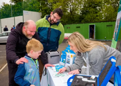 A woman shows energy awareness materials to a child at an outdoor event. Two men are also in the picture.